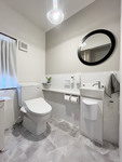 【改修後】石目調でシックな雰囲気に丸鏡と照明が印象的なトイレ空間は清掃性にもこだわり手洗カウンターの取り付く腰壁にホーローパネルを設置。ここでもマグネット小物が大活躍しています